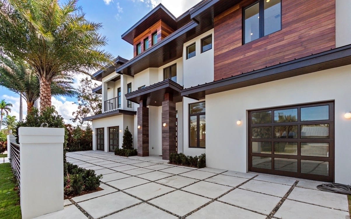 A modern South Florida home with impact windows, glass garage doors, and a paver driveway.